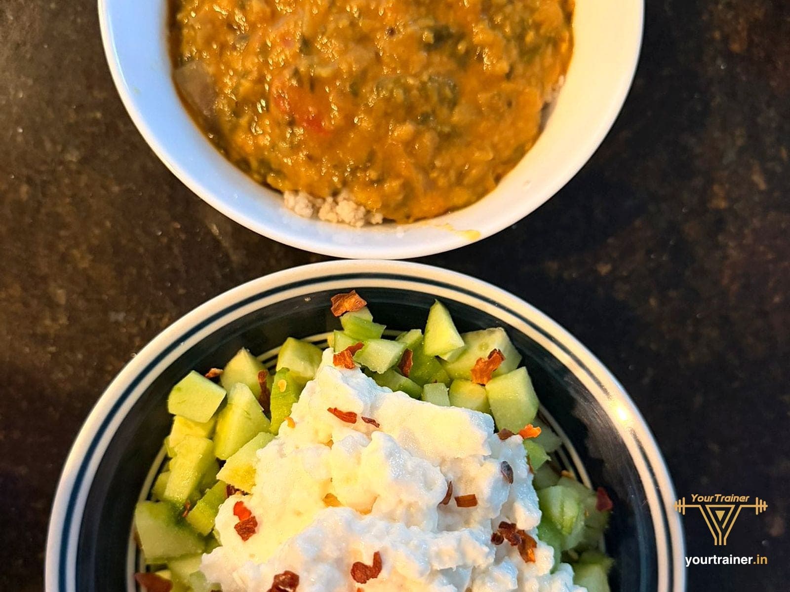 A bowl of dal and a bowl of cucumber with curd and chilli flakes