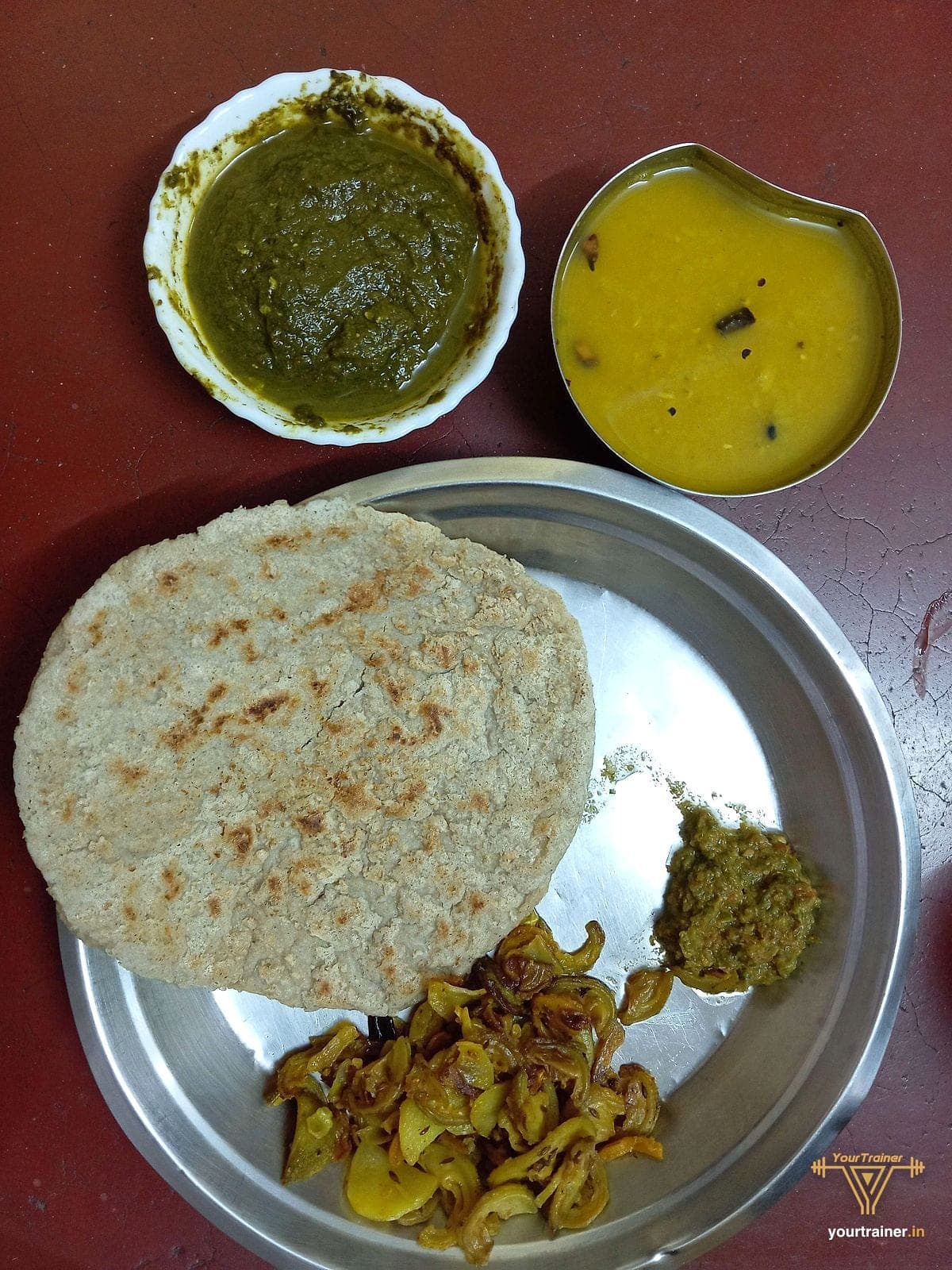 Millet roti with dal, a green saag, a dry sabzi and chutney on a steel plate