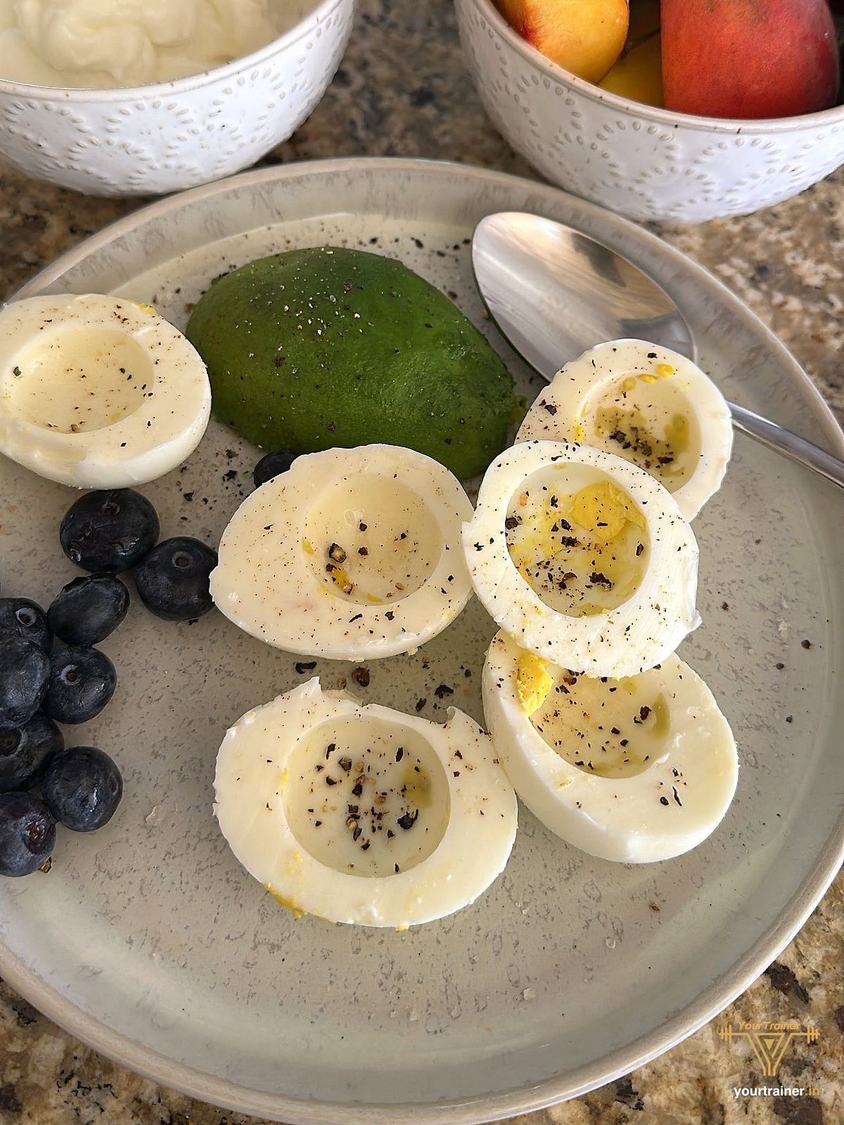 Member plate of halved boiled eggs with black pepper, half an avocado and blueberries