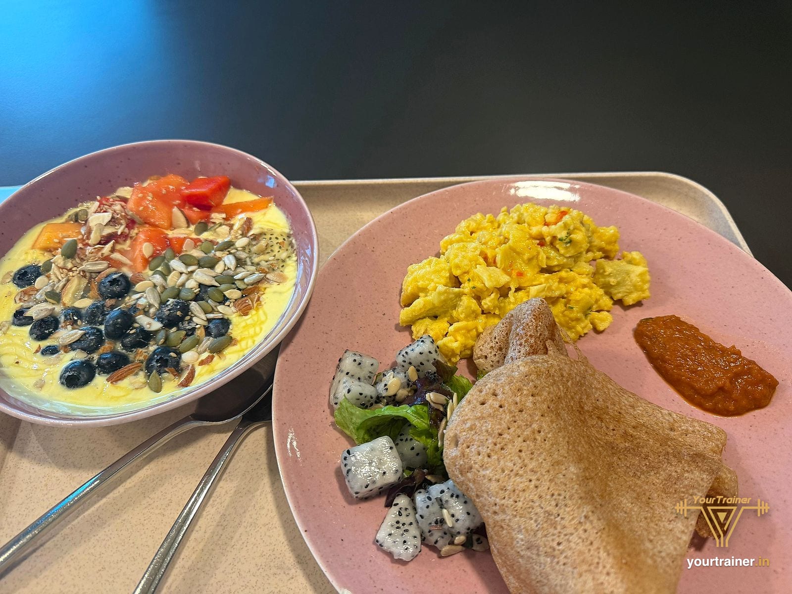 Tray with a dosa, scrambled eggs, dragon fruit salad, red chutney and a yogurt bowl topped with seeds and berries