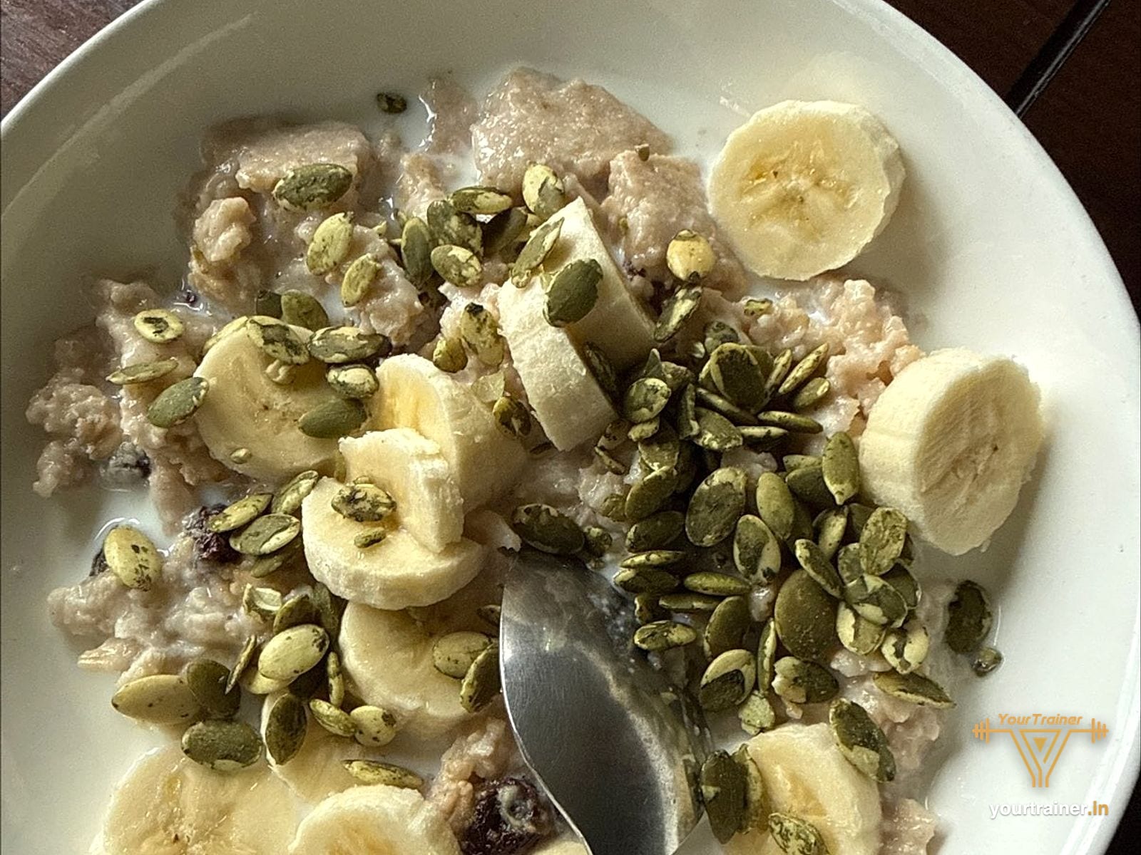 Bowl of oats topped with banana slices and pumpkin seeds