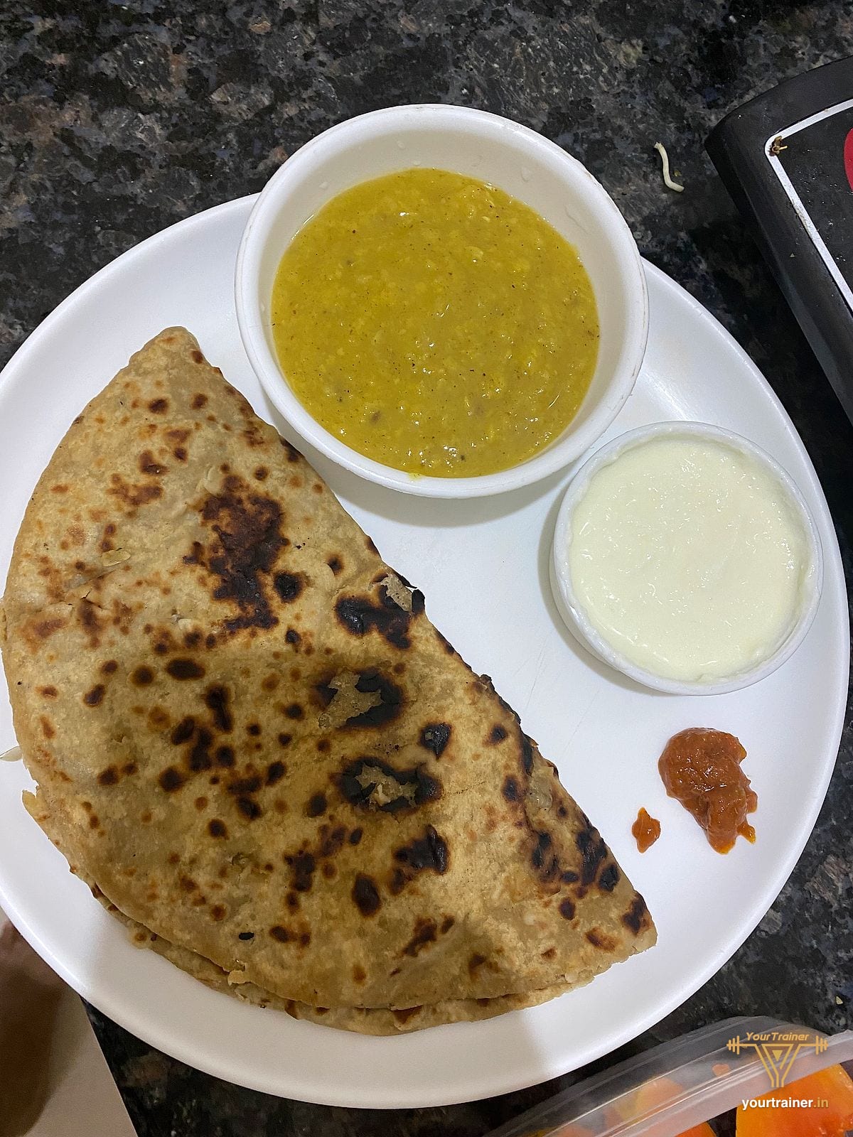 Paratha folded on a plate with a katori of dal and a small bowl of curd