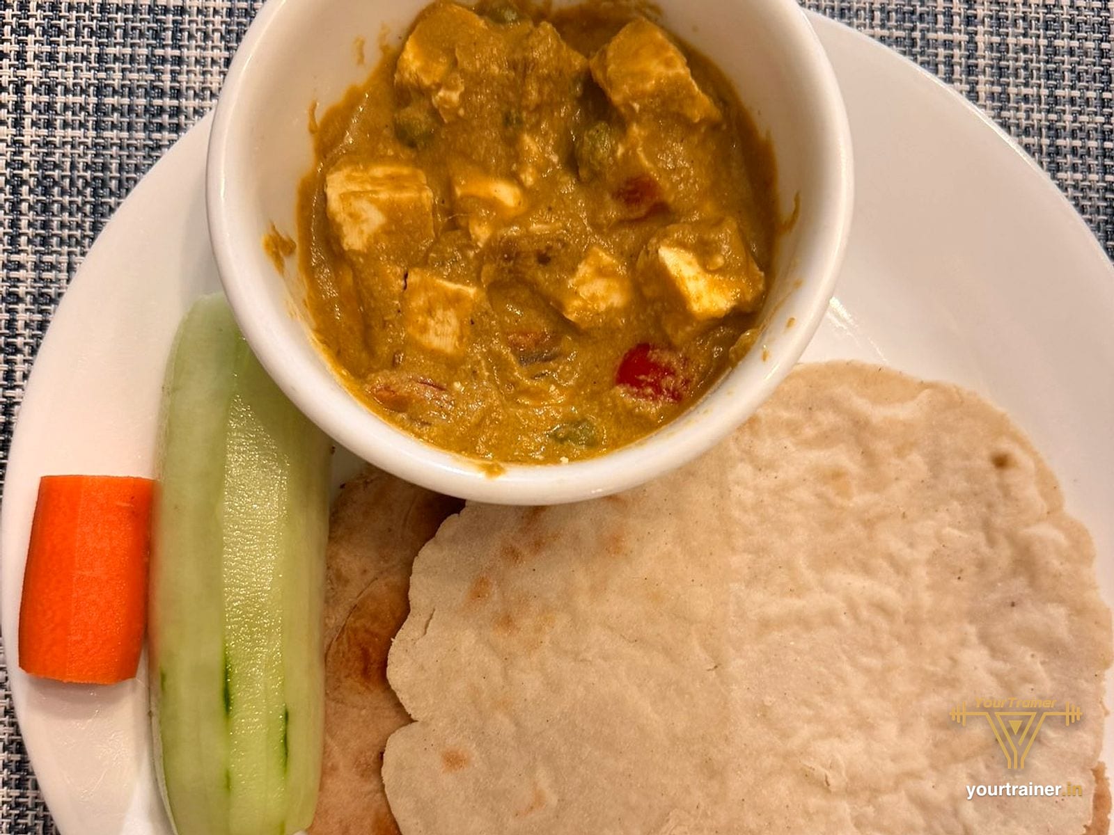 Phulka with a bowl of paneer curry, carrot and cucumber sticks