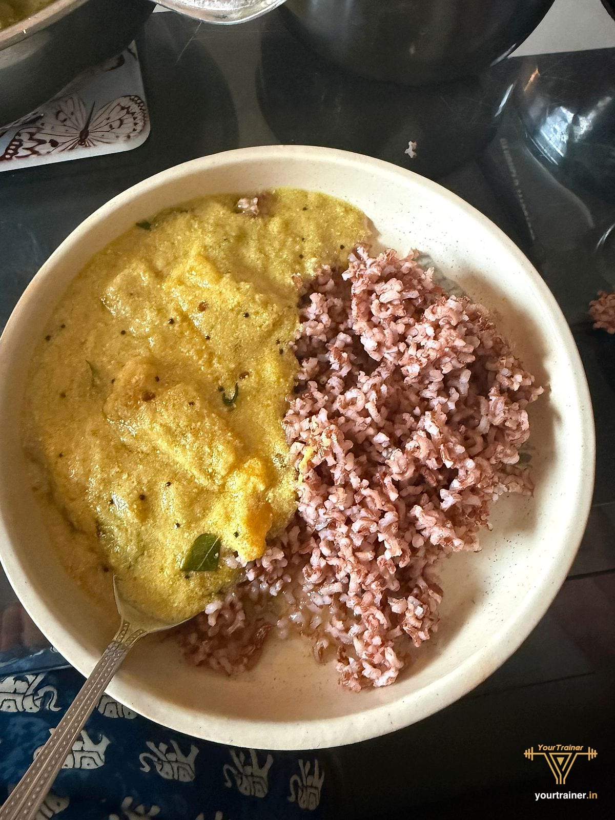 Bowl of red rice with a yellow coconut-style curry tempered with mustard seeds and curry leaves