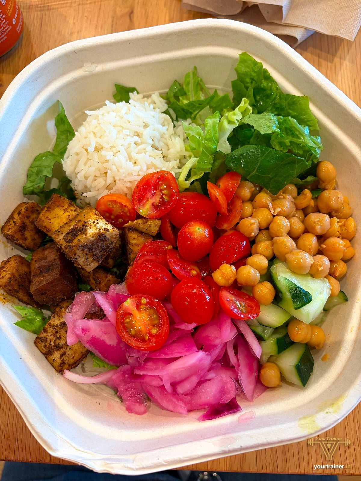Bowl of rice, lettuce, chickpeas, cherry tomatoes, cucumber, pickled onion and spiced cubes