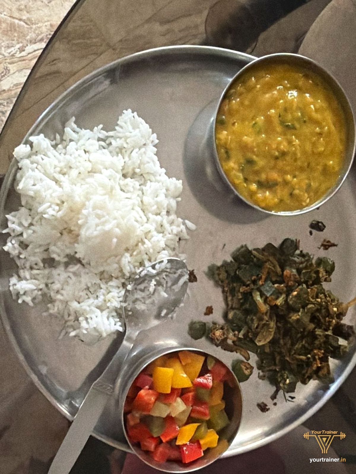 Steel thali with white rice, a katori of dal, bhindi sabzi and a katori of chopped salad
